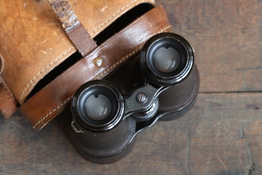 Closeup of old binoculars and leather case on wooden background