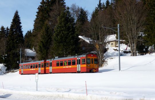 Red small train in Jura mountain by winter time