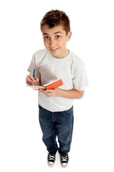 Full length boy jotting down notes in a small book or diary.  He is looking up from the book.  He is casually dressed in blue denim jeans and a plain grey t-shirt and smiling.  Shadows under feet.