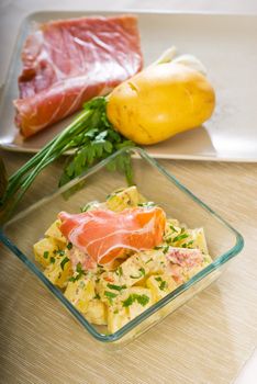 fresh home made parma ham and potato salad,with raw ingredients around with bowls and dishware on a table