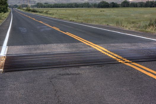 cattle guard across asphalt highway in Colorado with meadows and hills in background