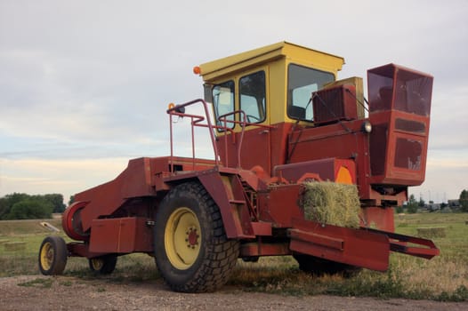 a small square hay baler in a field after harvest, HDR image