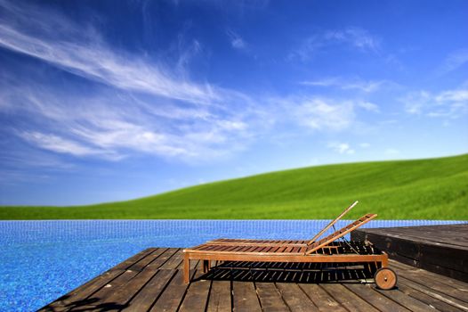 Beautiful outdoor space with a chair beside the pool and a beautiful green meadow  in the background