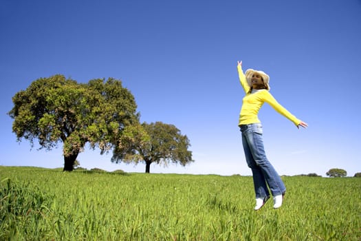 Haapy woman jumping on a beautiful green meadow with trees