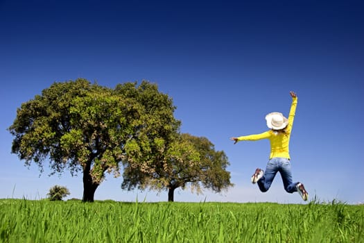 Haapy woman jumping on a beautiful green meadow with trees