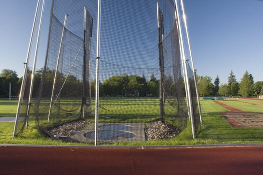 green grass athletic field with a hammer throw cage and long jump sand pit, early morning light