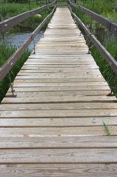 suspended footbridge over a small river, emphaisis on pathway with wooden rough planks