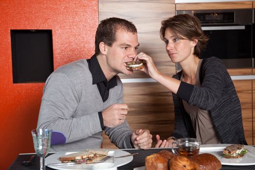 Pretty young couple having lunch together trying each others sandwich