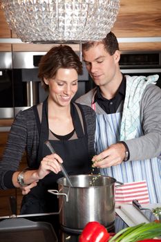 Man and woman together cooking in the kitchen, man adding something to the pan