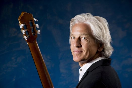 Classical Guitarist with his Instrument in front of a Blue Wall