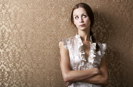 Pretty young woman waiting leaning up against a wall with gold wallpaper