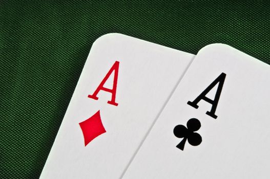 Close up of the top corner of two overlaying ace playing cards arranged on a dark green cloth.