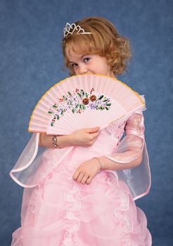 Beautiful little girl in a pink dress with a fan in his hand