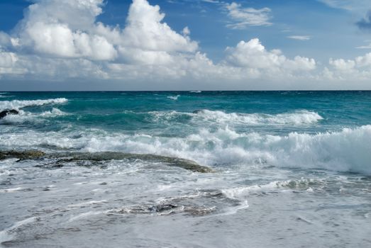 Beach with dramatic sea wave under blue sunny sky.
