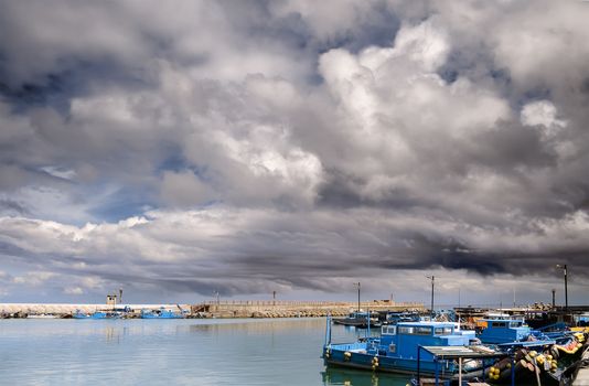 Boats on harbor under dramatic sky with storm clouds.