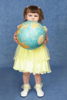 Little girl holding a large globe on a blue background