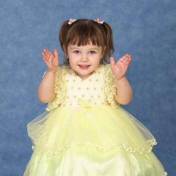 The little girl in a beautiful dress claps his hands on a blue background