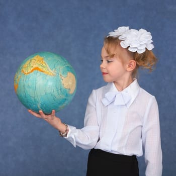 Schoolgirl looking at a geographical globe on a blue background