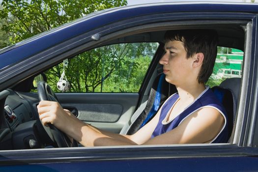 A young man smiling as he sits in a blue car