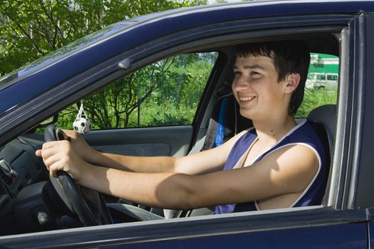 A young man smiling as he sits in a blue car