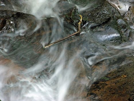 Water swirls around a lone stick over a waterfall.
