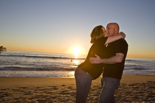 Young Pregnant Couple on the Beach at Sunset