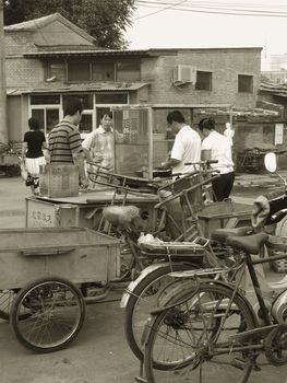 Black and white picture of a typical street scene in China. Before going to work people buy something to eat in a street food shop. This picture was taking in a Beijing hutong (traditional downtown ancient quarter)
