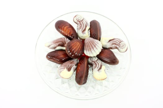 Sweet chocolate candies in the form of marine shellfish on glass plate isolated on white