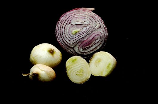 A sliced red onion surrounded by smaller yellow onions, on a black (000000) background.