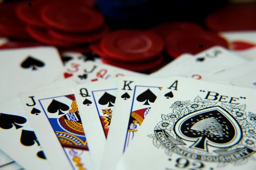 A royal flush poker hand shown face up over a pile of assorted cards and poker chips