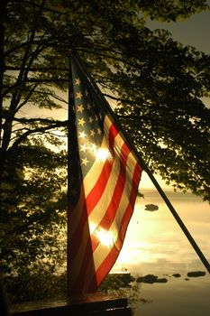 The sun sets across south-twin lake in millinocket Maine behind an american flag on memorial day.