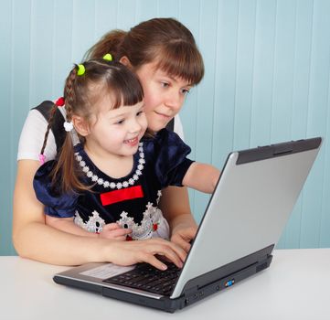 Mother and daughter playing with laptop sitting at the table