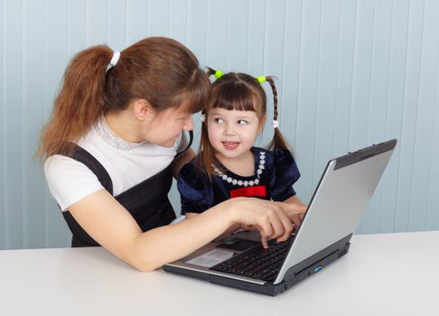 Mother and daughter playing with laptop sitting at the table