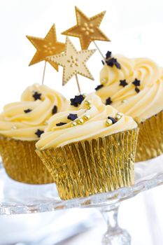 Three golden cupcakes on a glass cake stand