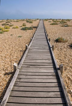 A raised wooden boardwalk across a pebble beach