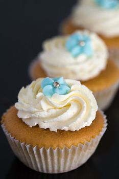 Cupcakes decorated with whipped cream and blue sugar flowers