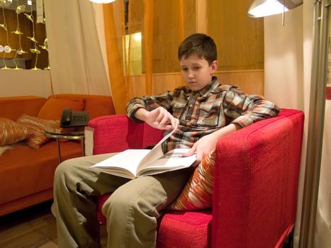 The boy sitting in a red armchair and reading the book