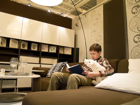 The boy on a sofa with white bear toy and reading the book