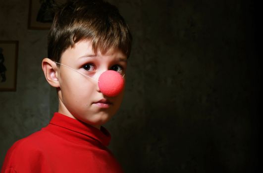 The upset boy with clown's nose in dark room