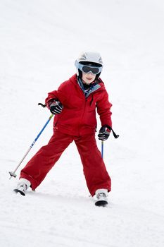Smiling young boy skiing down a snowy slope