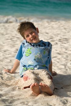 Young boy smiling on a beach, legs covered in sand