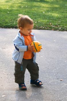 Walking baby holding orange ball at sunny day