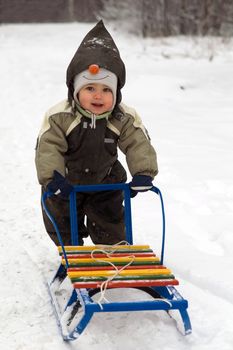 Baby in green coat pushing sled in snow-covered park