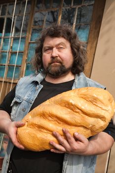 Man with big loaf of bread near country house