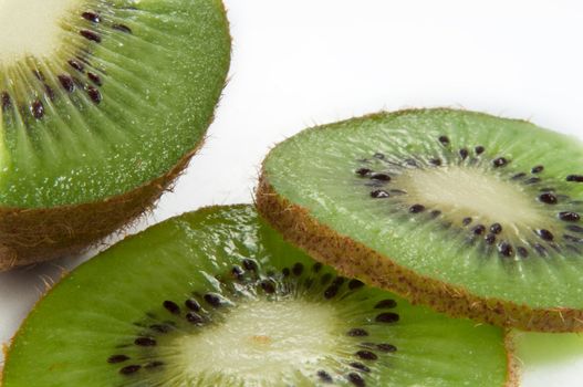 Close up and low level angle of a partially sliced fresh kiwifruit arranged over white.