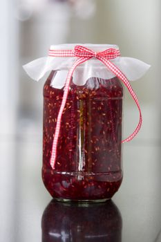 Jar of home made raspberry jam tied with a gingham ribbon