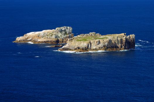 Two isolated and uninhabited rocky islands in the deep blue sea, off the coast of Tasmania, Australia. Space for text on the sea.