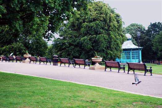 A photograph of a park with benches, a bandstand, and a pigeon taking flight