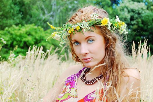 Beautiful girl with flower diadem among fields