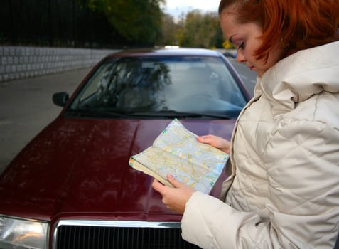 The young girl with a map of streets on a background of the red automobile